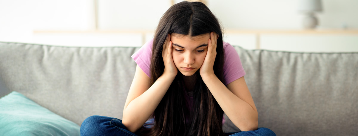 Eine junge Frau mit sorgenvollem Ausdruck hält sich mit beiden Händen den Kopf.